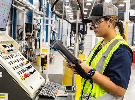 white female employee in a hardhat holding a tablet and stylus while looking at a piece of machinery